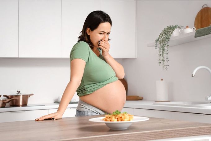 a pregnant woman standing in a kitchen with a plate of food