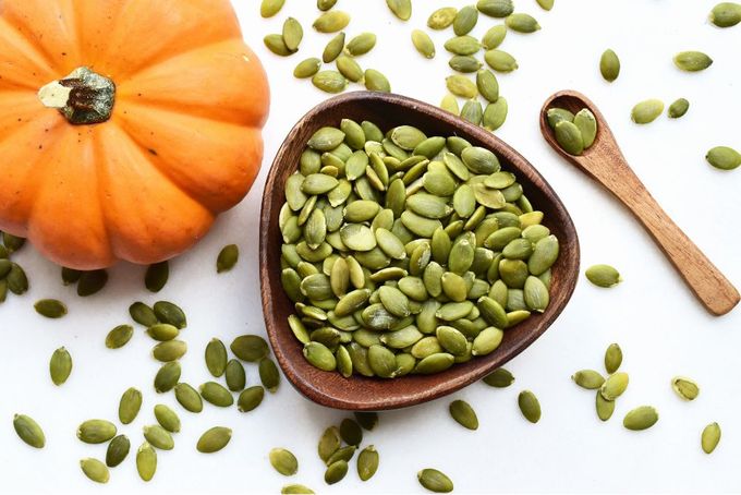 a wooden spoon filled with pumpkin seeds next to a pumpkin