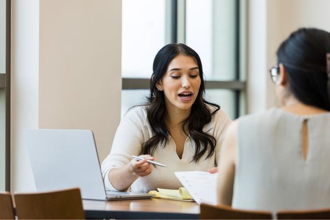 two women sitting at a table with a laptop