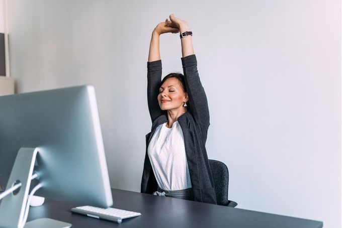 a woman sitting at a desk with her arms in the air