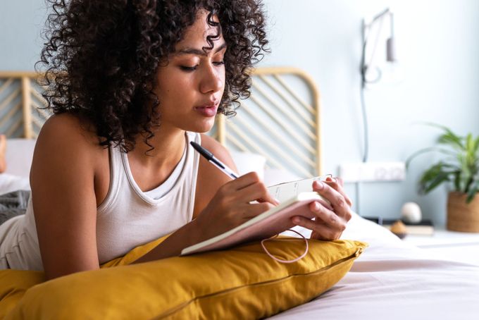a woman sitting on a bed writing in a journal, keeping track of her period and symptoms