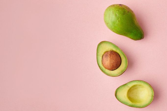 an avocado cut in half on a pink background