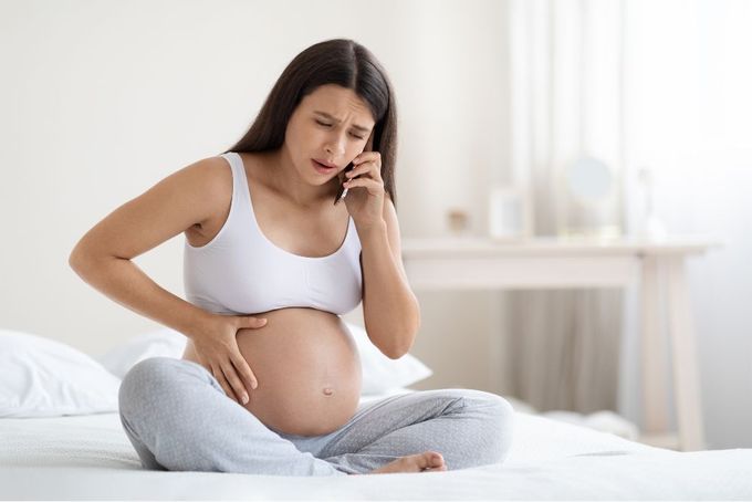 a pregnant woman sitting on a bed talking on a cell phone