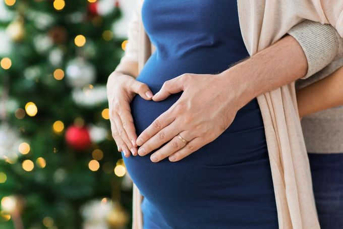 a pregnant woman holding her belly in front of a christmas tree