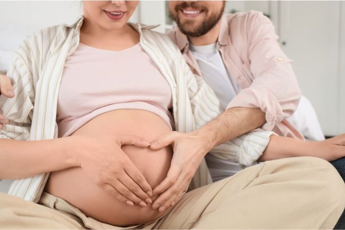 a pregnant woman sitting on a bed next to a man