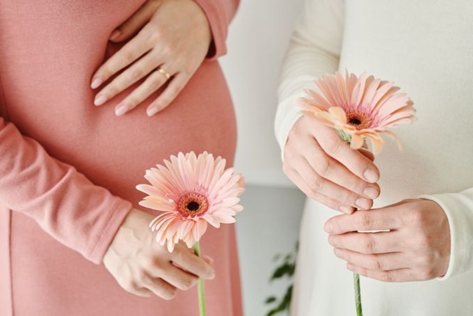 a pregnant woman holding a pink flower next to a pregnant woman