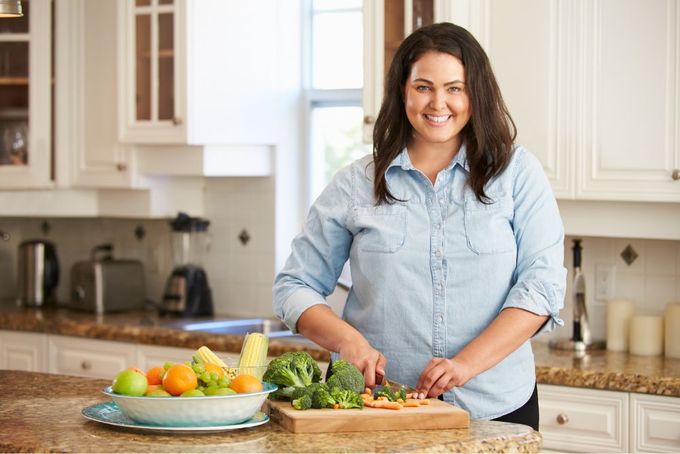 a woman standing in a kitchen cutting vegetables