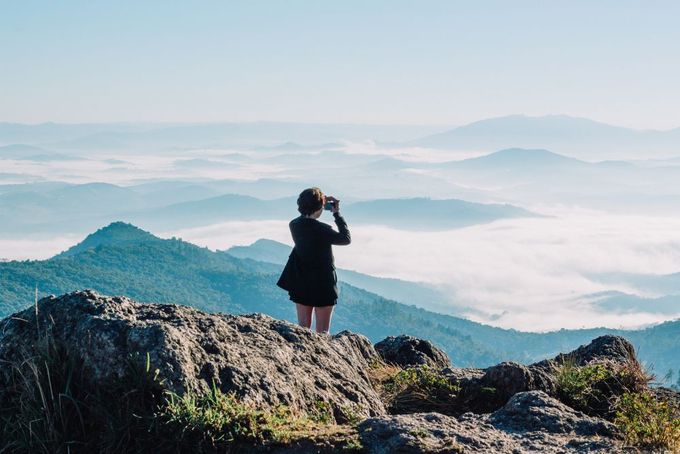 a woman standing on top of a mountain taking a picture