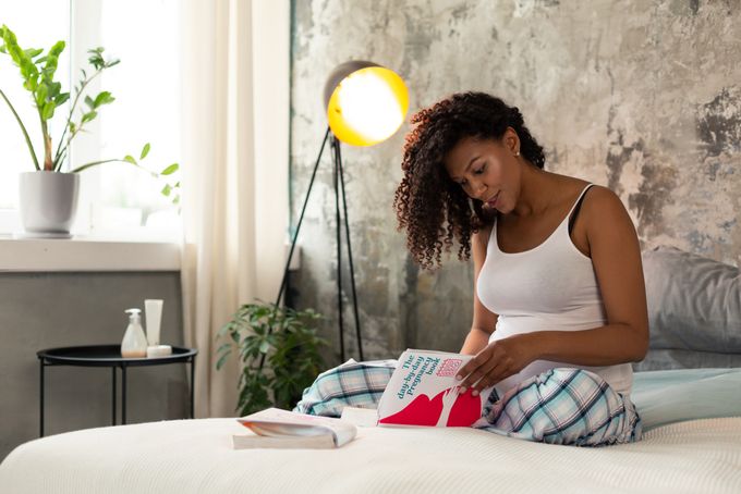 a woman sitting on a bed reading a book about pregnancy after 35, planning and preparing for a baby