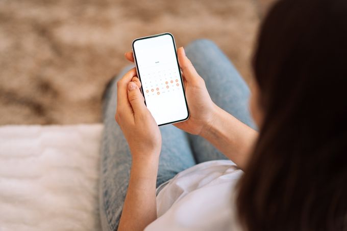 a woman sitting on a couch holding a cell phone and looking at a calendar