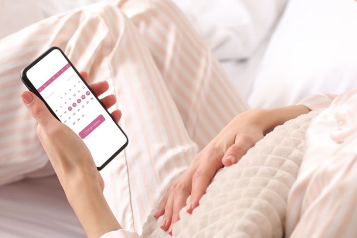 Woman holding a phone, looking at her period calendar that tracks her cycle, symptoms, and fertility window.