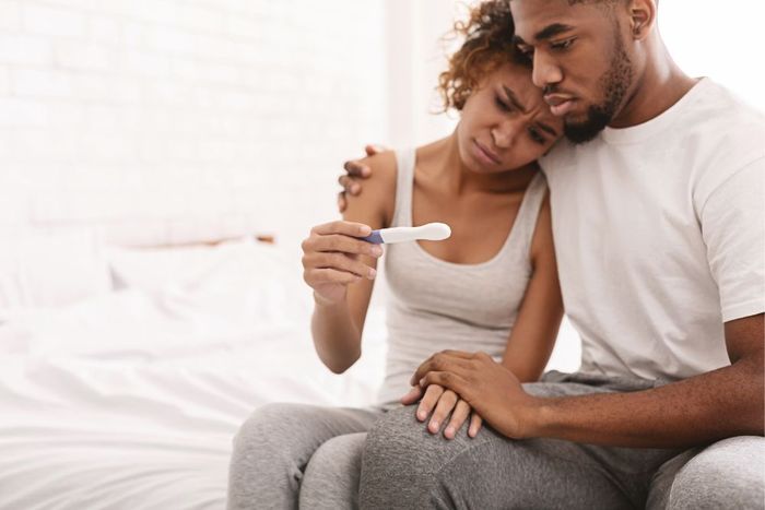 a man and woman sitting on a bed looking at a toothbrush