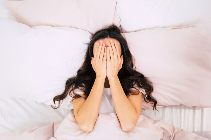 a woman laying in bed covering her face with her hands