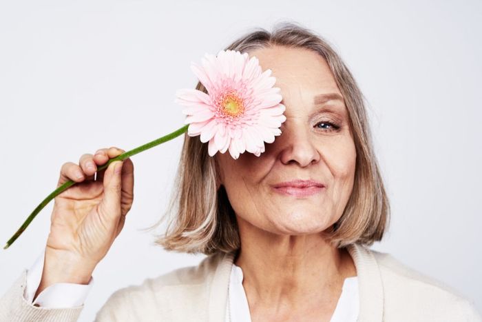 a woman holding a pink flower in front of her face