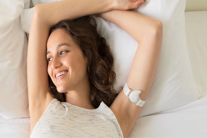 A woman in bed wearing a BBT thermometer on her arm.