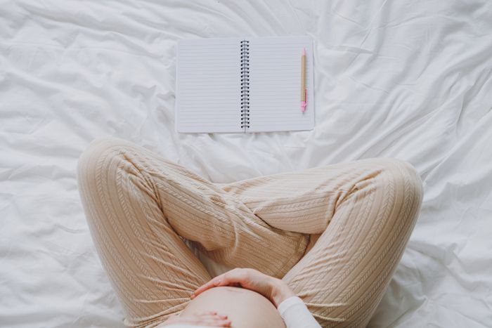 a pregnant woman laying on a bed with a notepad tracking her pregnancy
