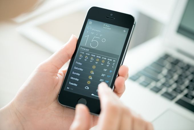 A person holding a cell phone and checking their weather app