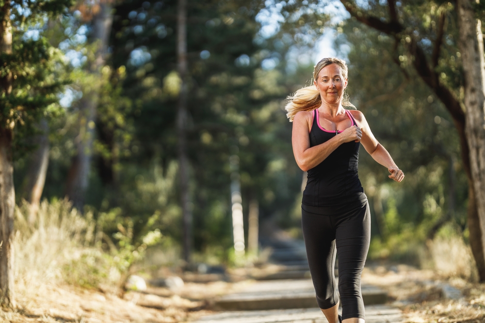 Middle-aged blonde woman in workout clothes running outside