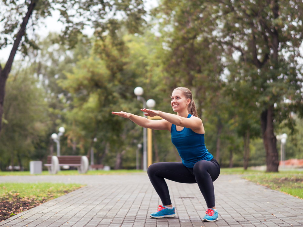 Woman doing squats in a park wearing exercise clothes and smiling