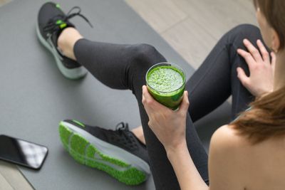 Woman sitting and holding a green detox smoothie in one hand