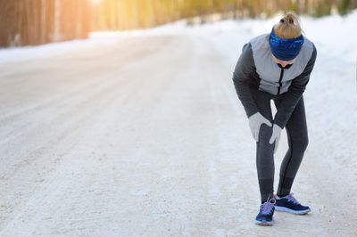 Woman in workout clothes on a snowy road holding her knee in pain