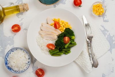 A plate with fish, veggies, and a side of rice next to a fork on a table