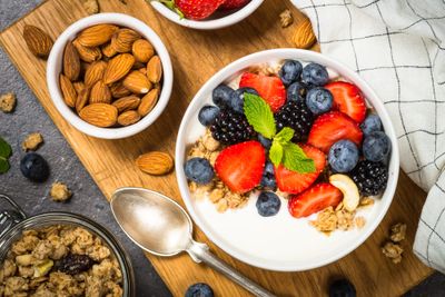 A bowl of yogurt with berries next to a bowl of almonds on a wooden board