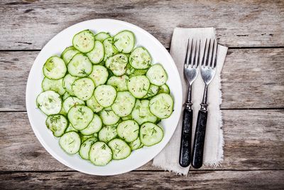 Top view of a plate with cucumber salad next to utensils on a wooden table