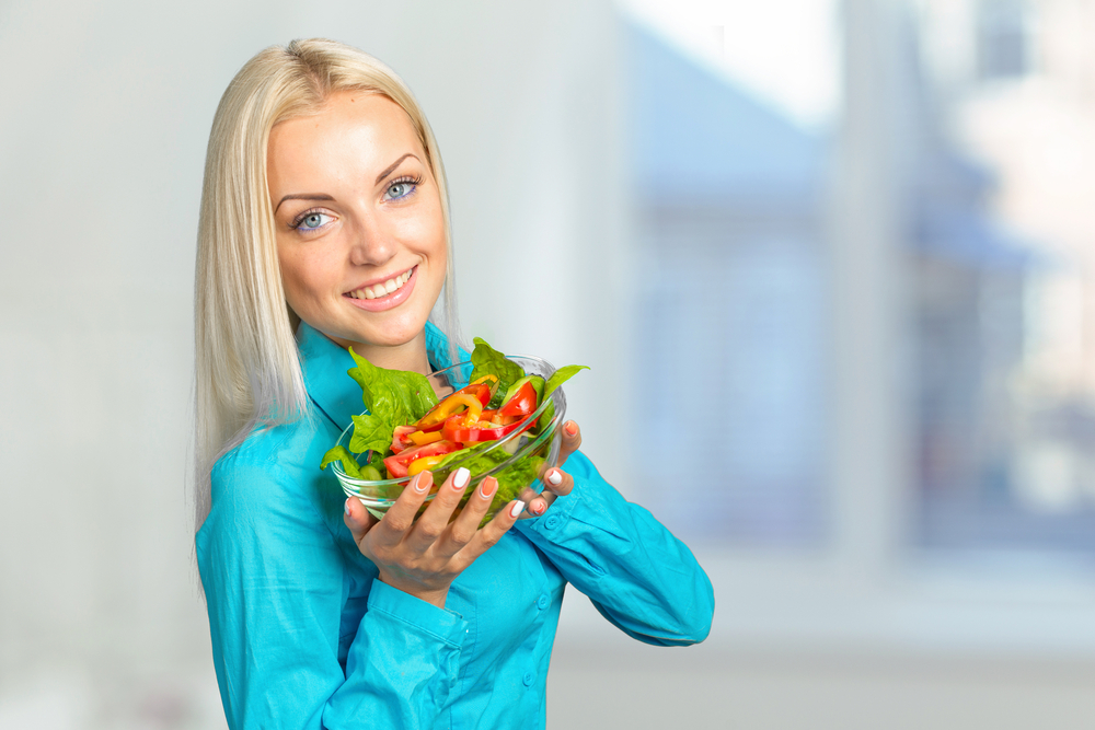 Blonde woman smiling and holding a bowl with salad