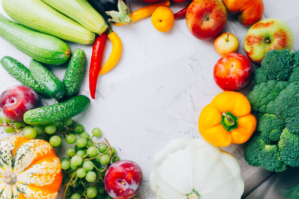 Different colorful fruits and vegetables arranged in a circle on a white cloth