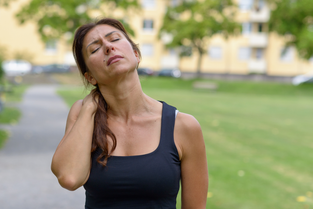 Woman holding her neck suggesting soreness in workout clothes