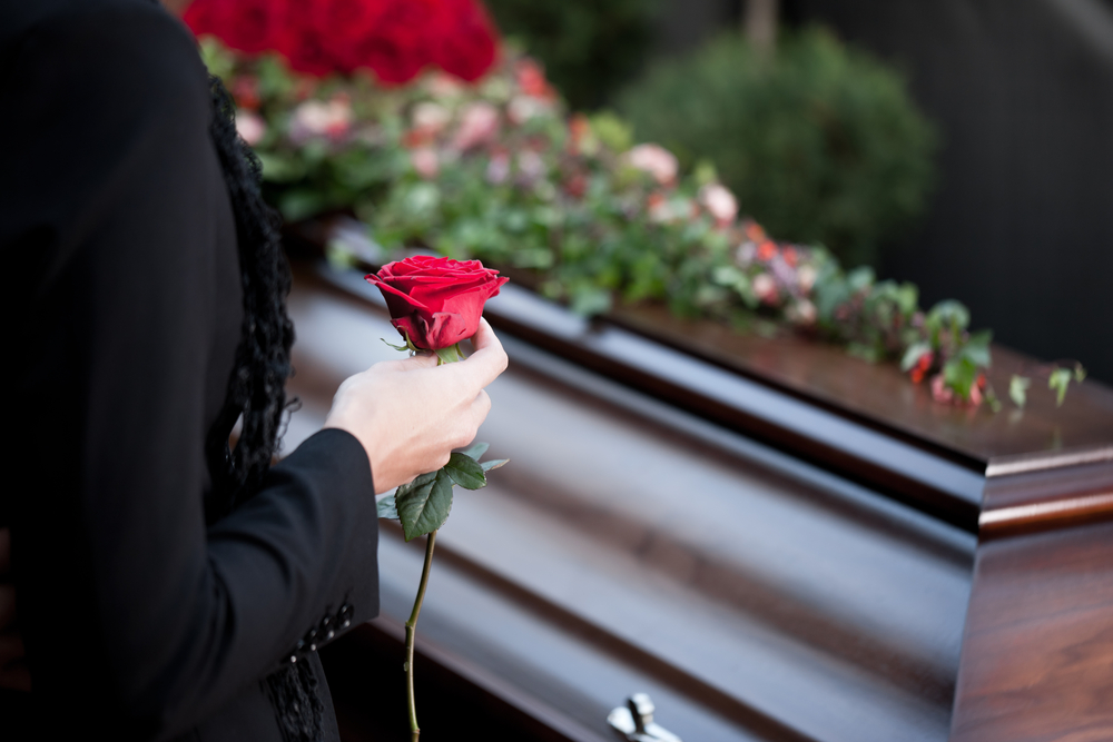 Woman holding rose next to coffin with flowers on it