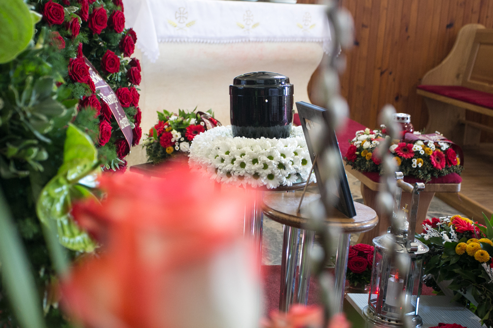Black urn on table surrounded by flowers and picture frames