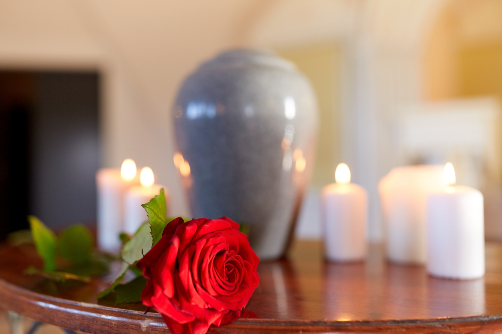 Blue urn on wooden table surrounded by burning candles and a red rose