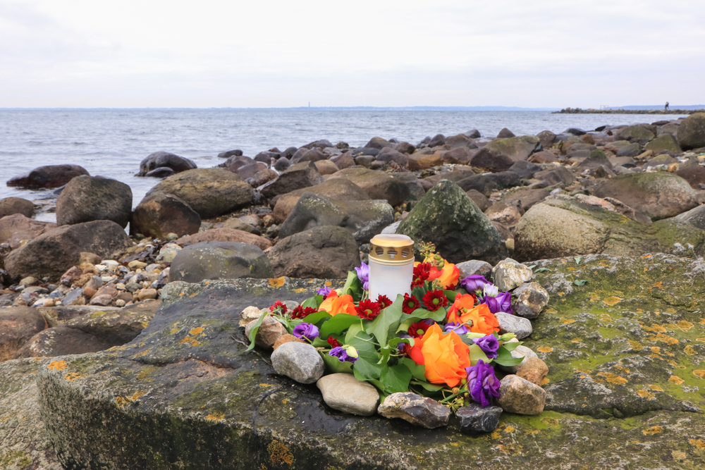 flowers and glass urn stacked on green rock by the ocean