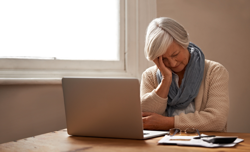 Elderly lady looking at laptop screen hanging her head in her hands