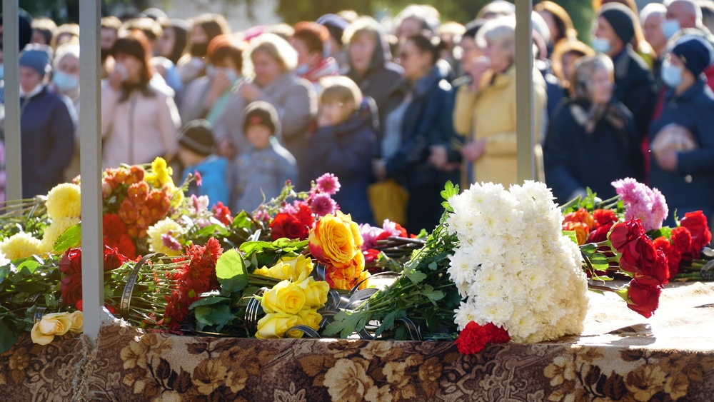 People outside gathered behind coffin topped with flowers