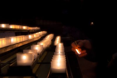 Person lighting a candle standing in front of four rows of candles