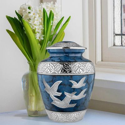A marble dark blue urn with silver bird detailing in front of a vase with flowers