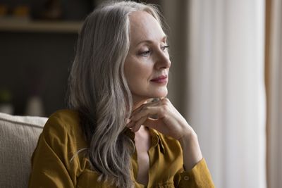Elderly woman with grey hair sitting on couch and staring off in contemplation