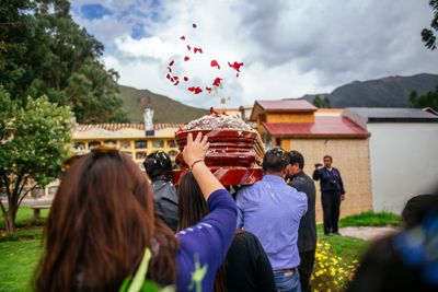 Men in suits carrying coffin with flowers being thrown into the air around them