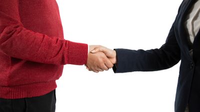 Man in suit shaking hands with man in red jersey