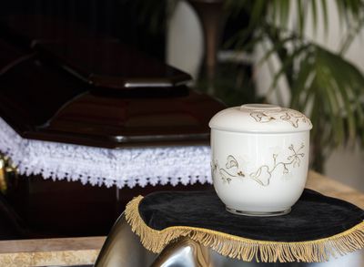 White urn on black tablecloth next to coffin