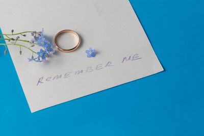 The bottom-half of a page on a bright blue background. On the page, a few delicate blue flowers, a ring, and the handwritten words "remember me".