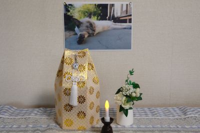 Colorful urn, candle, and flowers on tablecloth beneath picture of a cat