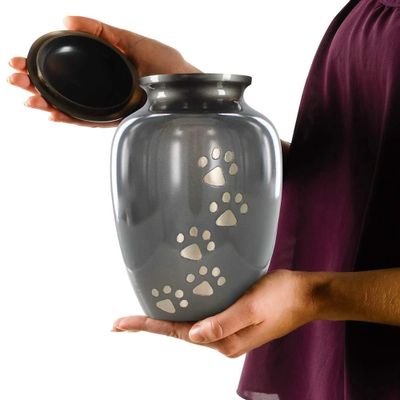 A person holding an open gray pet urn with paw prints on the front