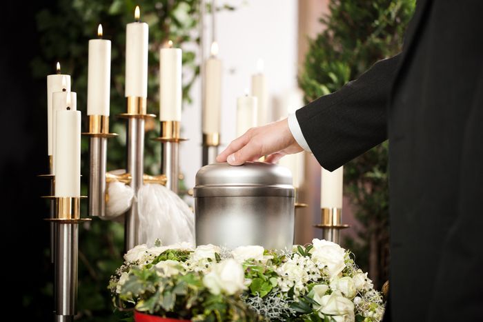 Man placing hand on metallic urn surrounded by flowers and candles
