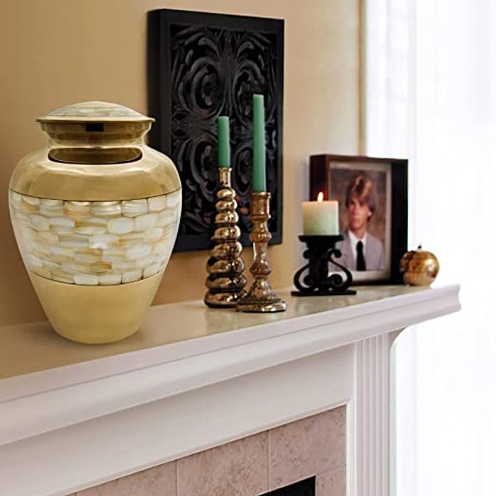 A stunning cremation urn placed on top of a fireplace display, along with a photograph and assortment of candles.