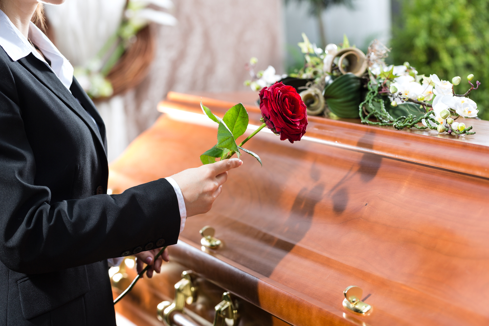 Woman in black suit placing red rose onto coffin