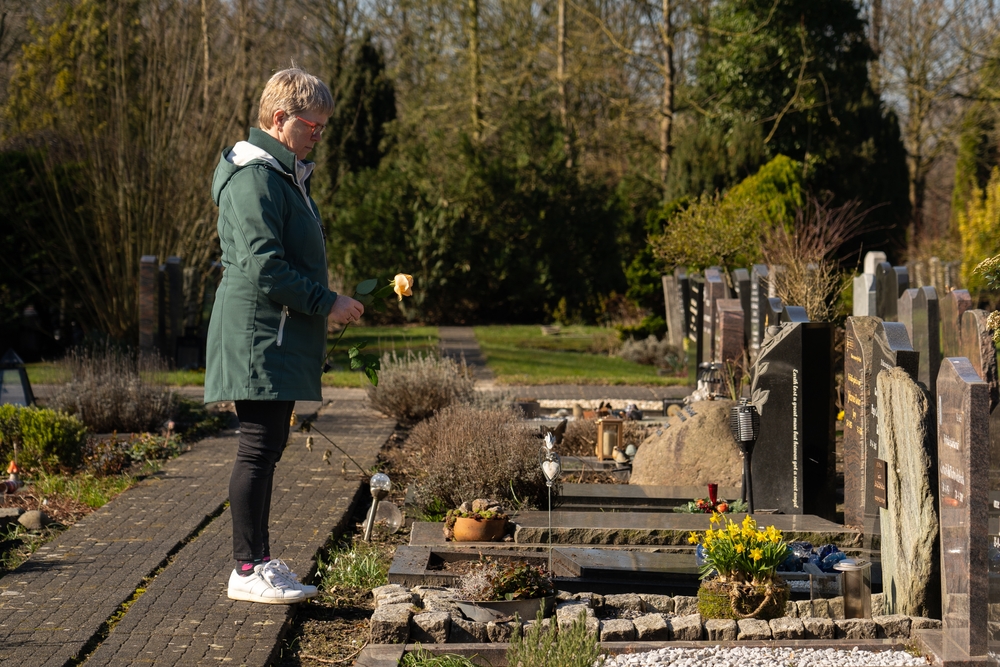 Woman standing near gravestones holding yellow rose